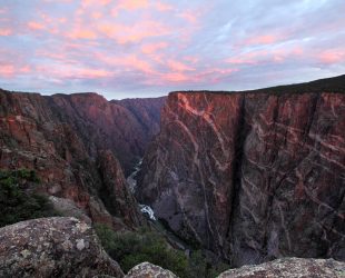 Sun rises over Black Canyon of the Gunnison, Colorado. This cliff is the Painted Wall, the tallest vertical cliff in Colorado, at 2,722 feet. Sunlight barely peeks through the clouds to brighten the top of the cliff with a touch of sunlight.